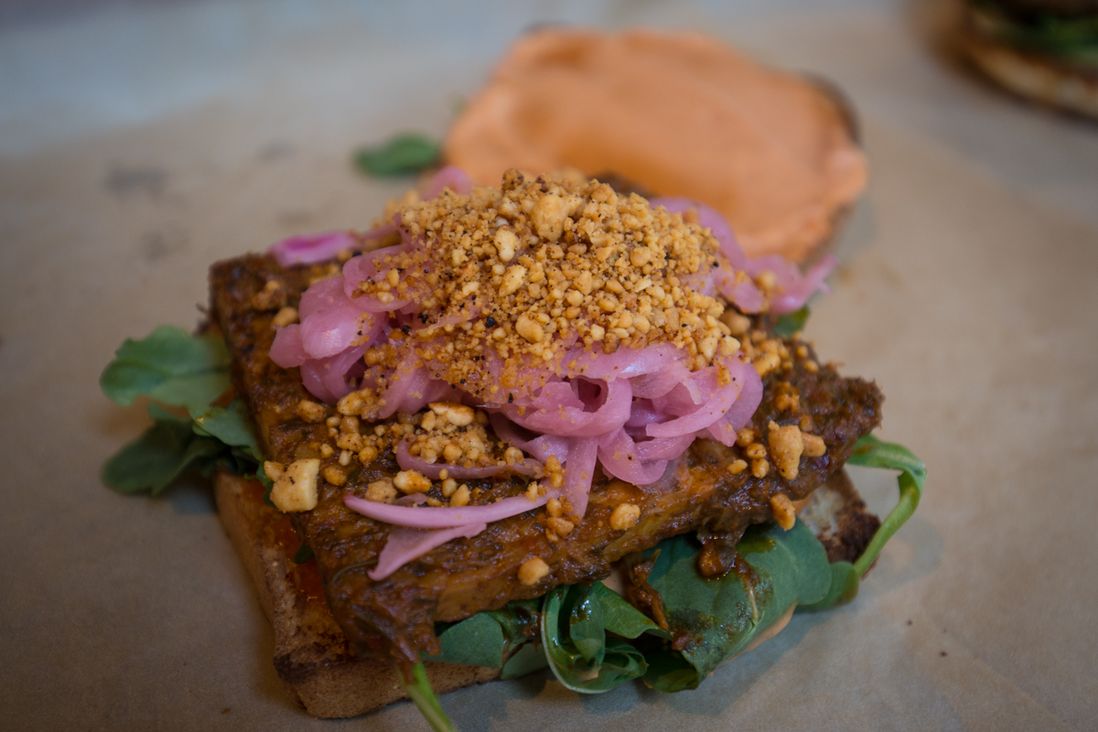 Thai BBQ Tempeh - ($12) with smoked chili roasted peanuts, pickled red onions, baby arugula & sriracha mayo on grilled spelt bread from Cinnamon Snail<br>